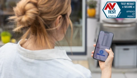 Eine Frau mit der ABUS One App auf ihrem Smartphone und der AV Test Siegel © ABUS