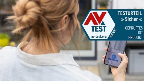 Eine Frau mit der ABUS One App auf ihrem Smartphone und der AV Test Siegel © ABUS