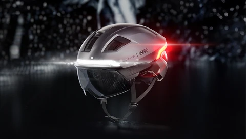 Produktfreisteller des HYP-E Urban-Fahrradhelms in Gleam Silver mit integriertem Visier sowie leuchtendem Front- und Rücklicht © ABUS