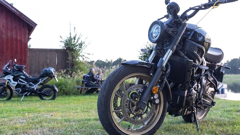 Au premier plan, une moto sécurisée par un verrou de disque de frein. À l'arrière-plan, une deuxième moto et deux personnes assises sur un banc. ©ABUS