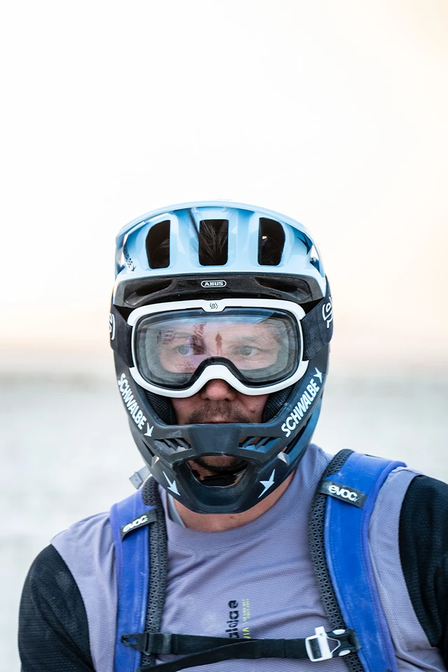 A mountain biker wearing a helmet and goggles looks directly into the camera © ABUS