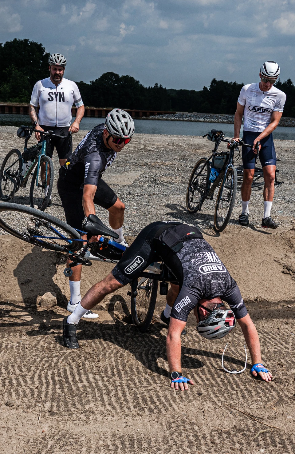 Des cyclistes sur route aident un membre de leur équipe après avoir traversé une zone de gravier. © ABUS