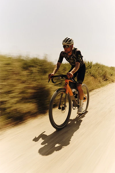 Paul Voss porte un casque Taipan Gravel ; il roule sur un chemin de gravier poussiéreux à travers un paysage aride. © ABUS