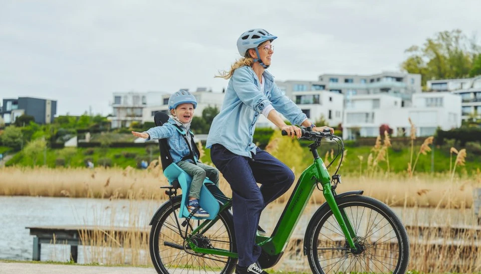 A woman rides a bicycle with a child seat along the lake © ABUS