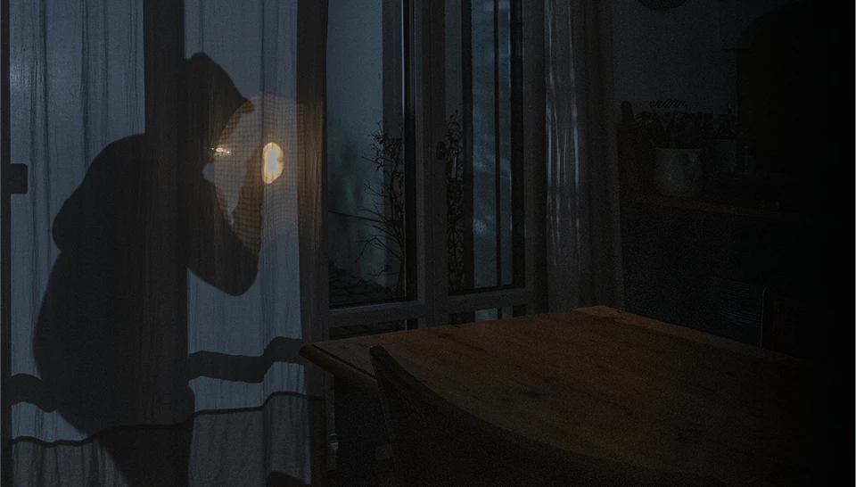 Ein Einbrecher, links im Bild, späht von der Terrasse mit einer Taschenlampe in die Wohnung.