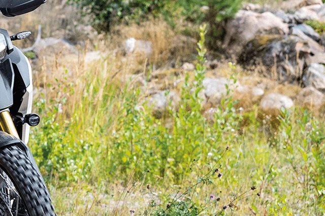 Ein Fahrer in schwarzer Motorradkombi fährt auf einer Enduro-Maschine von Triumph über einen Schotterweg im Gelände. ©ABUS