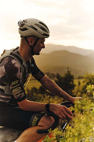 Paul Voss trägt Taipan Gravel-Helm und sitzt auf dem Fahrrad; blick bei Sonnenuntergang über eine hügelige Landschaft © ABUS