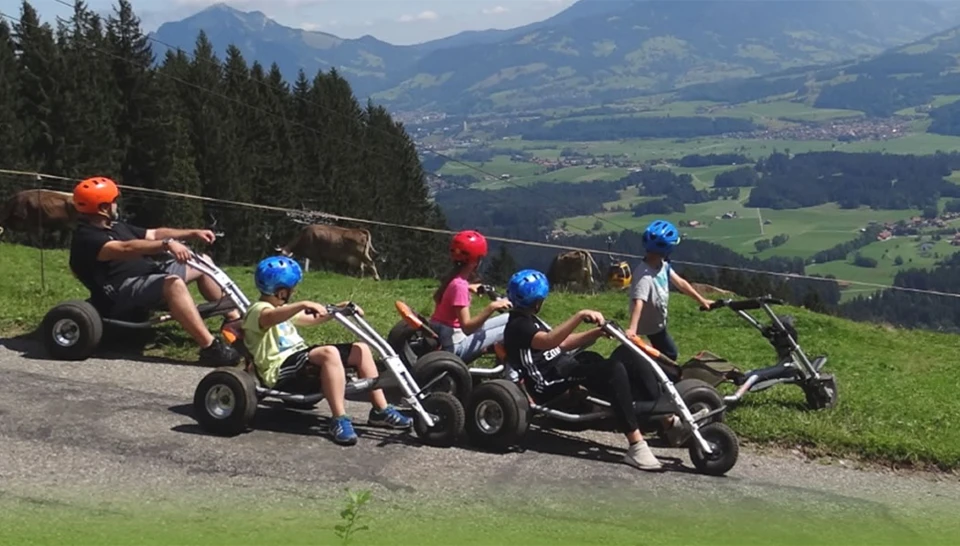 Gruppe von Kindern fährt mit Bergrollern durch Landschaft der Hörnerbahn