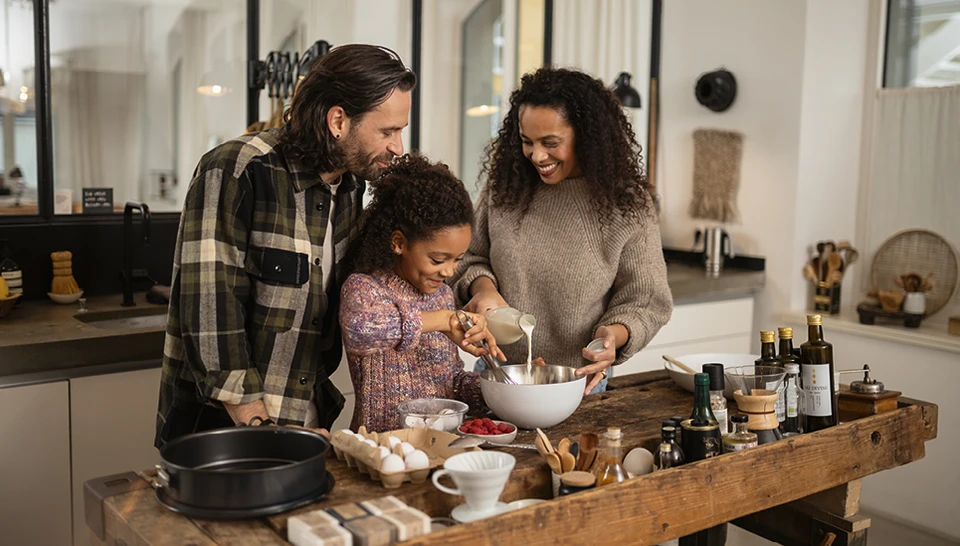 Familie steht gemeinsam einen Kuchen backend in der Küche.