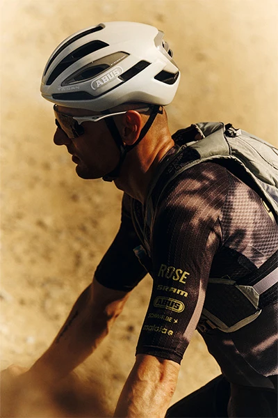 Seitliche Nahaufnahme Paul Voss mit Taipan Gravel-Helm während der Fahrt auf einem hellen, staubigen Trail © ABUS