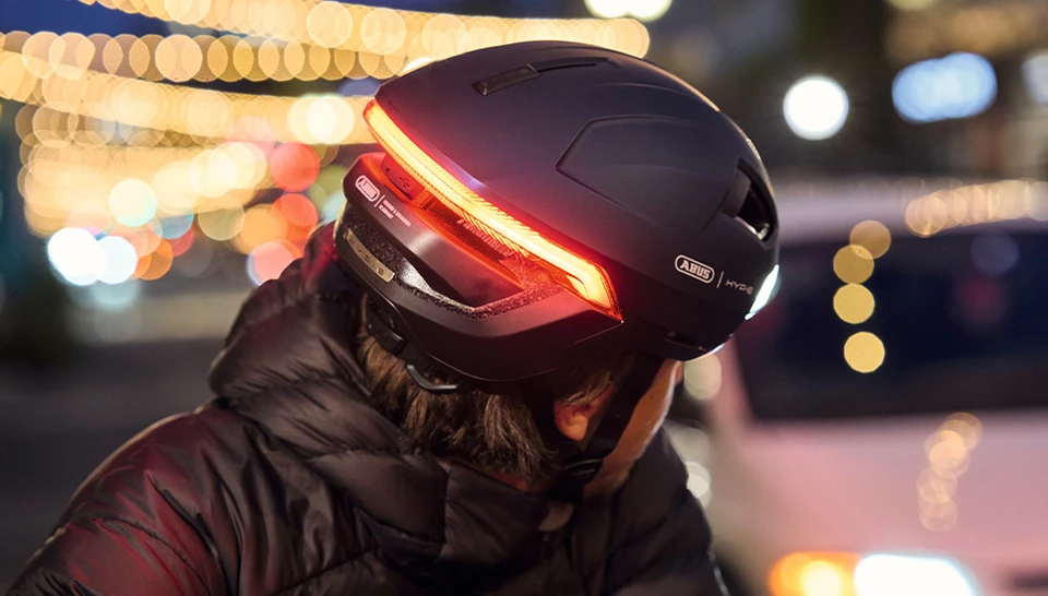 Man on a bicycle looks back and wears the HYP-E urban bicycle helmet in midnight blue. © ABUS