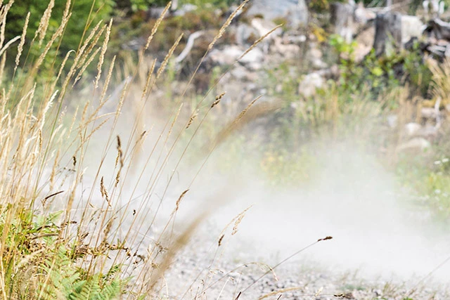 Ein Fahrer in schwarzer Motorradkombi fährt auf einer Enduro-Maschine von Triumph über einen Schotterweg im Gelände. ©ABUS