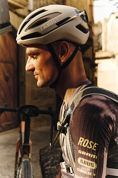 Primo piano laterale di Paul Voss con il casco Taipan Gravel, seduto sulla sua bicicletta in un vicolo illuminato da luci calde © ABUS