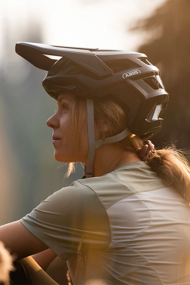 Mountainbikester kijkt naar de zonsondergang. Zijaanzicht met focus op de MTB-fietshelm Targon © ABUS