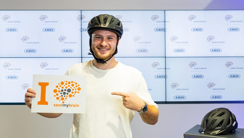 ABUS Mitarbeiter mit Fahrradhelm und einem Schild in der Hand mit claim "I savemybrain" &copy; ABUS