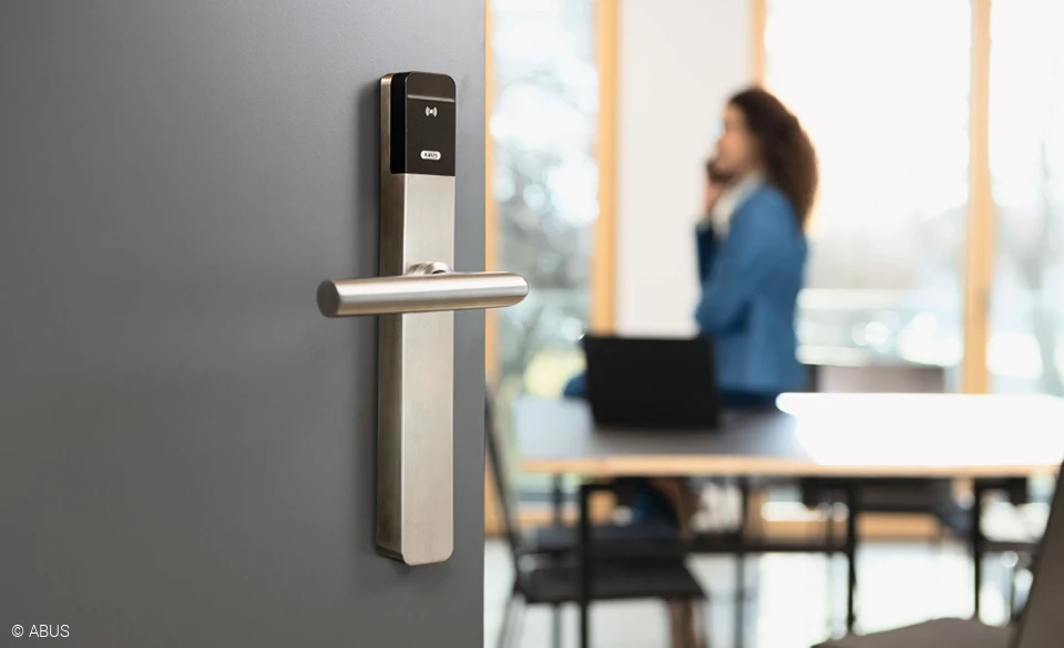 In the foreground, a modern office door with TECTIQ hardware. A woman on the phone in the background.