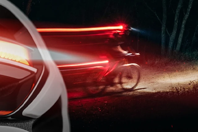Cyclist at night in the forest, red rear light of the Taipan bicycle helmet creates a trail of light © ABUS