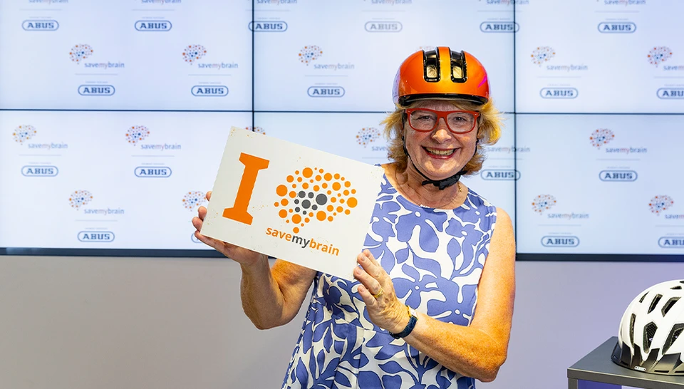 Frau tr&auml;gt urbanen Fahrradhelm HUD-Y in orange und h&auml;lt l&auml;chelnd Schild mit claim "I savemybrain" &copy; ABUS