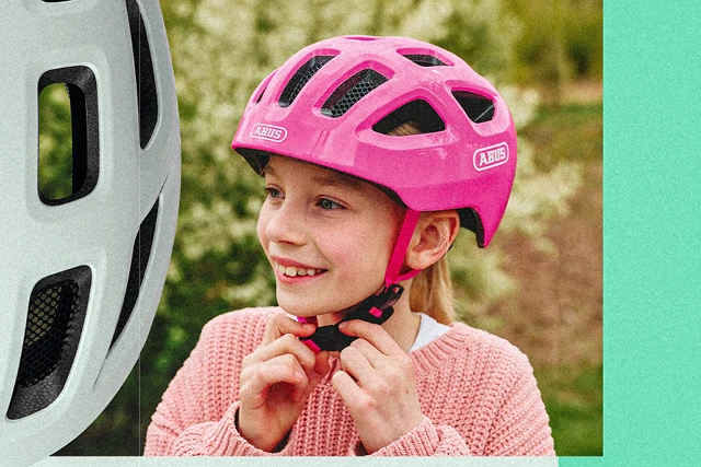 A girl wearing a pink Youn-I 3.0 cycle helmet as she fastens her chin strap © ABUS