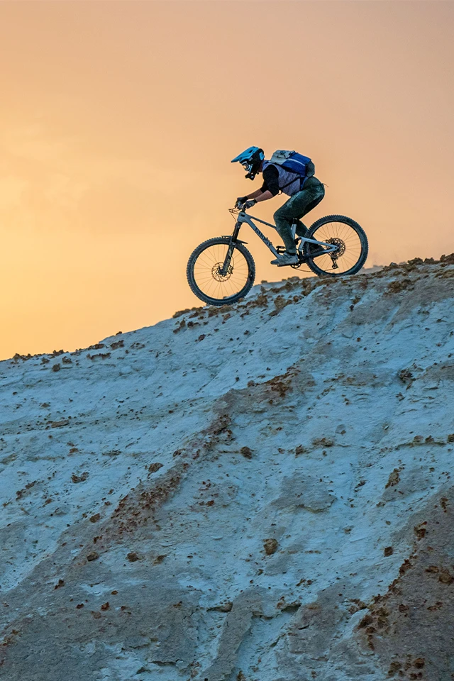 Mountainbiker fährt einen steilen Hügel bei Sonnenuntergang hinab © ABUS