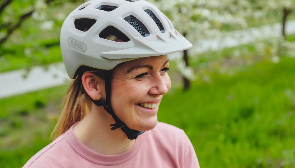 A woman looks to the side with a smile. She is wearing the YOUN-I 3.0 ACE in powder beige © ABUS