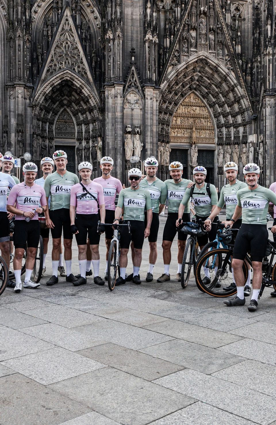 Gruppo di ciclisti agonistici in piedi con le loro biciclette davanti a una cattedrale storica © ABUS