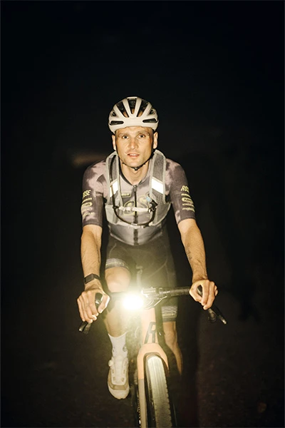 Paul Voss mit Taipan Gravel-Helm fährt nachts, frontal im Lichtschein der Fahrradlampe © ABUS
