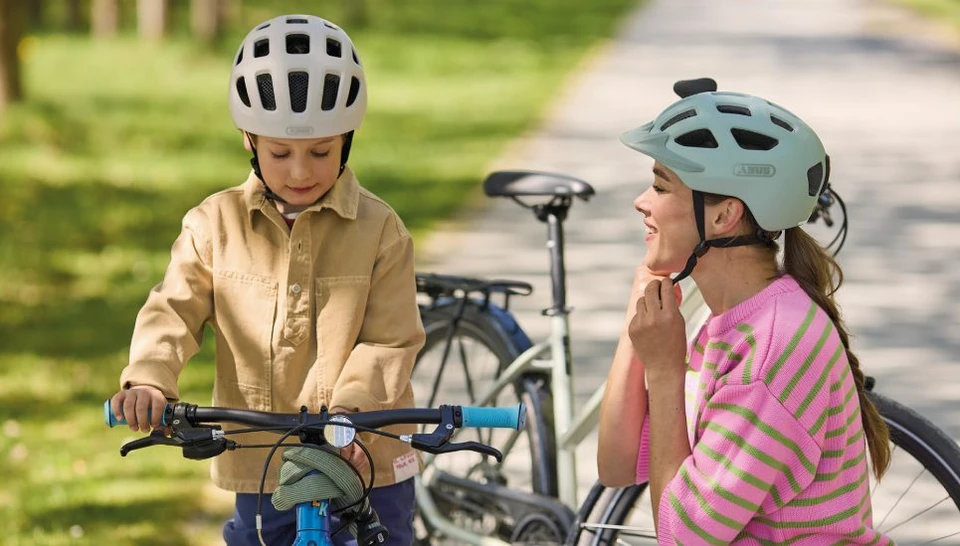 A woman and a young boy on a bike ride; she is fastening her YOUN-I 3.0 ACE cycle helmet © ABUS