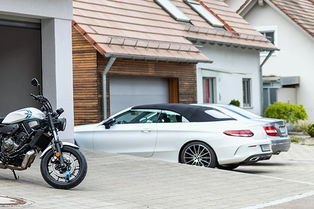Egy fekete motoros overallban lévő férfi kilép a házából, és odamegy a nyitott garázs előtt álló motorjához. ©ABUS
