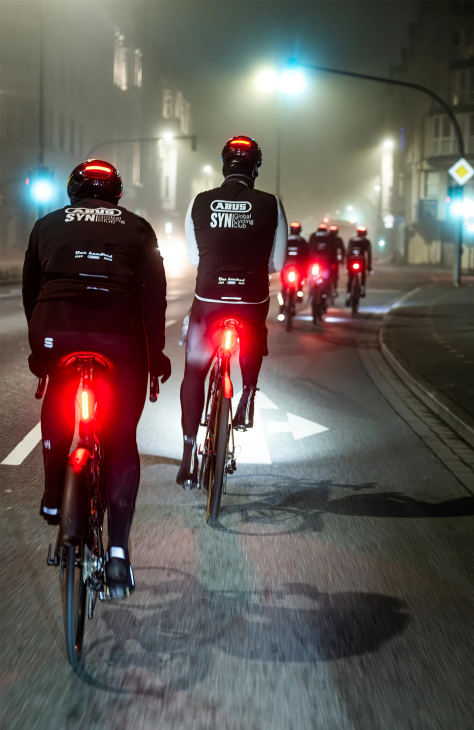 Road cyclists wearing Taipan LED bicycle helmets riding through the city at night, with integrated rear lights © ABUS