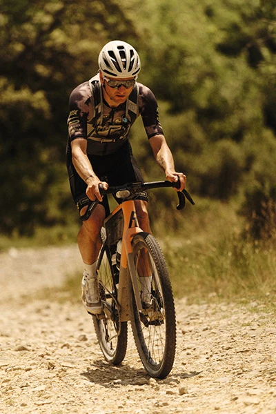 Paul Voss mit Taipan Gravel-Helm fährt einen steinigen Trail bergauf durch eine bewaldete Umgebung © ABUS