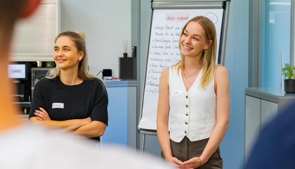 Zwei Mitarbeiterinnen stehen im Seminarraum vor einem Whiteboard und lächeln © ABUS