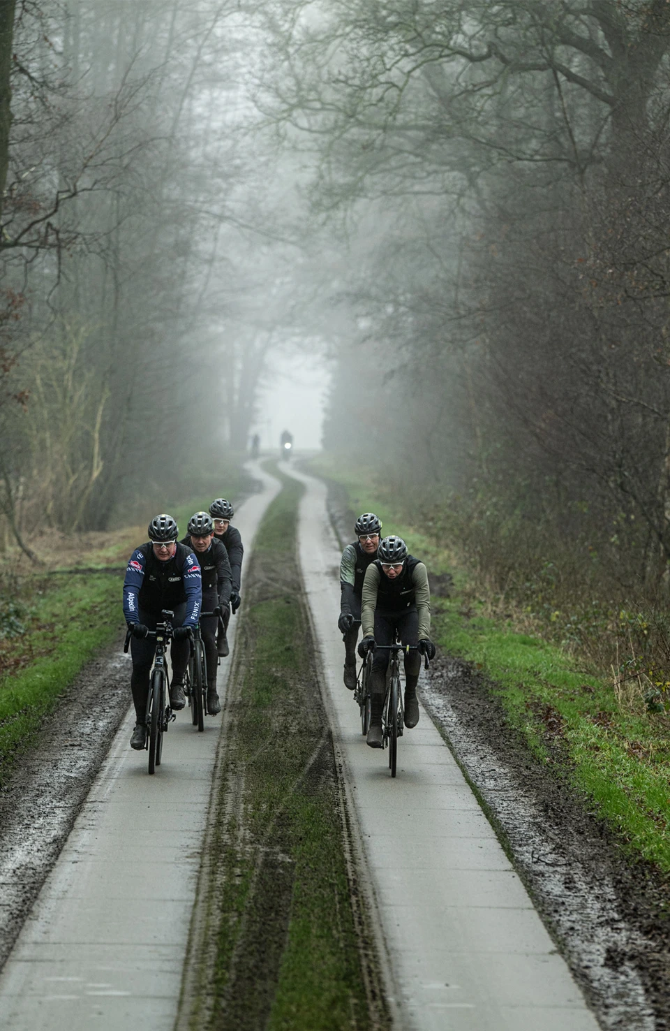 Several racing cyclists wearing Taipan bicycle helmets ride along a narrow concrete path through a misty forest. © ABUS