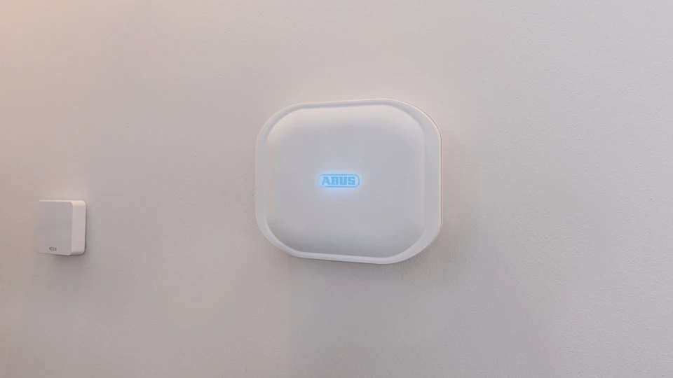 Comfion Pro control unit mounted on a white wall. The ABUS logo is lit up in blue.