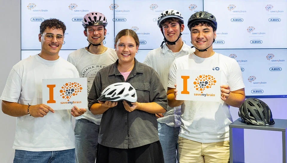 Vier ABUS Mitarbeiter nebeneinander mit Fahrradhelm und einem Schild mit claim "I savemybrain" &copy; ABUS