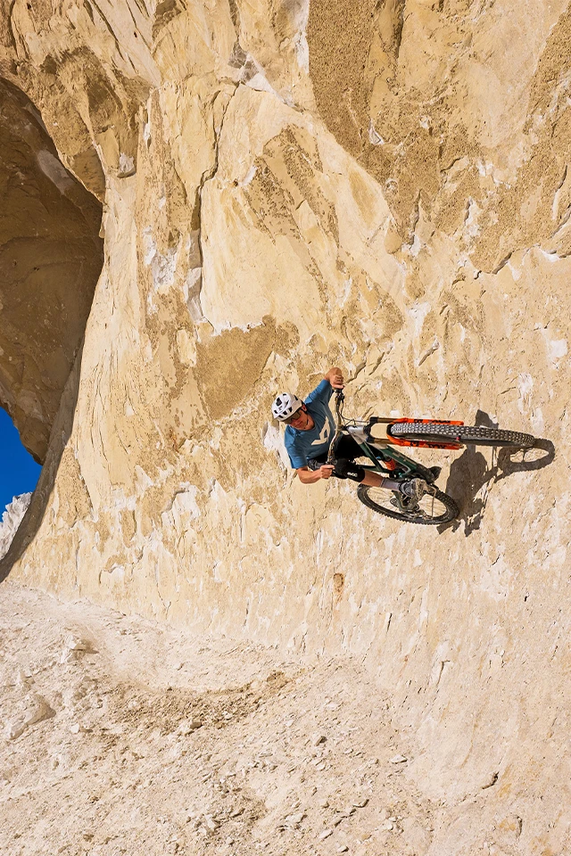 Mountainbiker fährt steile Felswand in heller Wüstenlandschaft entlang © ABUS