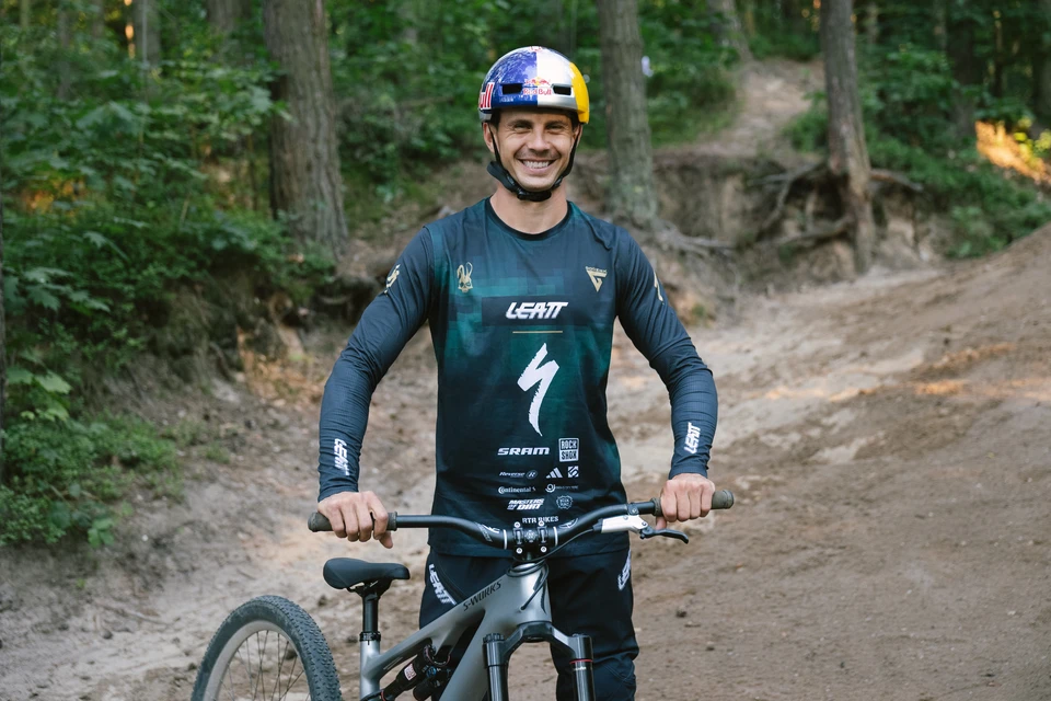 Szymon Godziek uśmiecha się do aparatu, siedząc na swoim rowerze górskim na leśnej ścieżce © ABUS
