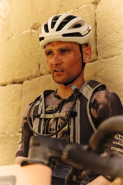 Paul Voss porte un casque Taipan Gravel ; épuisé, il s'appuie contre un mur de pierre. © ABUS