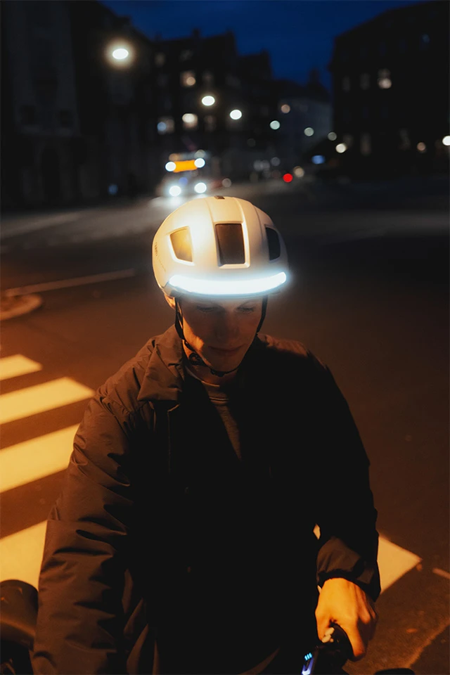 Ein Mann fährt bei Nacht Fahrrad und trägt den HYP-E Fahrradhelm mit leuchtendem LED-Frontlicht © ABUS