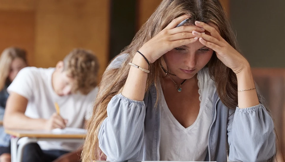 Mädchen sitzt mit gesenktem Kopf an einem Tisch in der Schule © ABUS