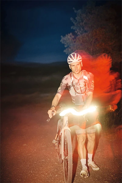 Paul Voss con il casco Taipan Gravel guida al buio, con sfocatura di movimento e luce anteriore luminosa © ABUS