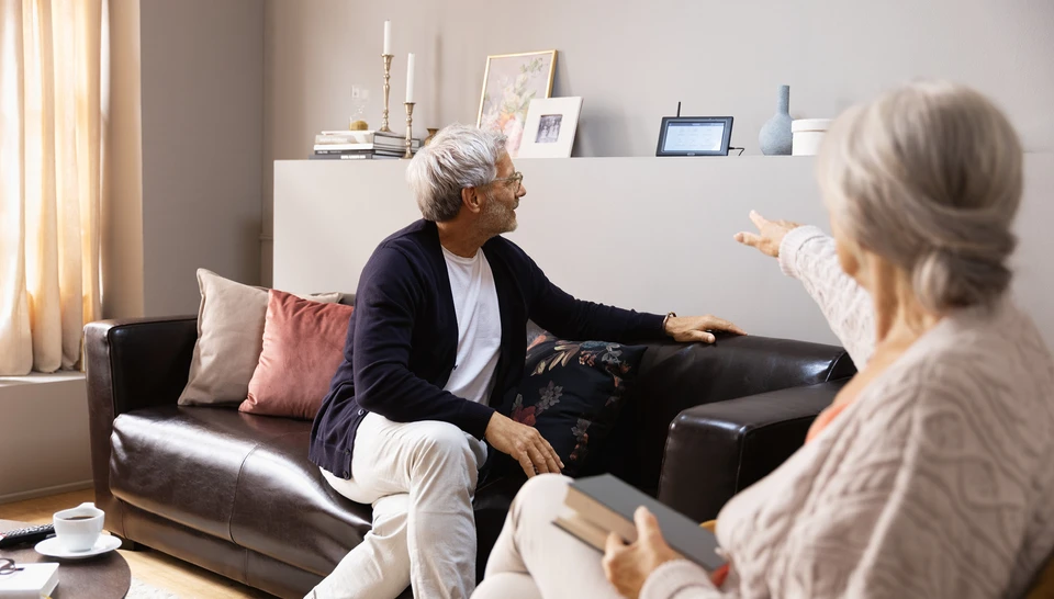 Ein älteres Paar sitzt auf einer Couch im Wohnzimmer und betrachtet gemeinsam den Monitor mit Einstellungen ihrer Videoüberwachungskamera.