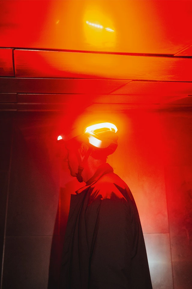 Man wearing a HYP-E bike helmet with glowing red rear light against a red background © ABUS