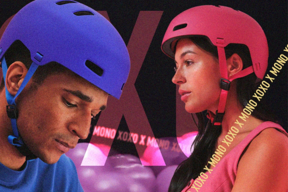Zwei Personen mit den Fahrradhelmen XOXO in den Farben Mono blue und Mono red  schauen nach unten bzw. zur Seite, vor Hintergrund mit XOXO X MONO-Schriftzug © ABUS