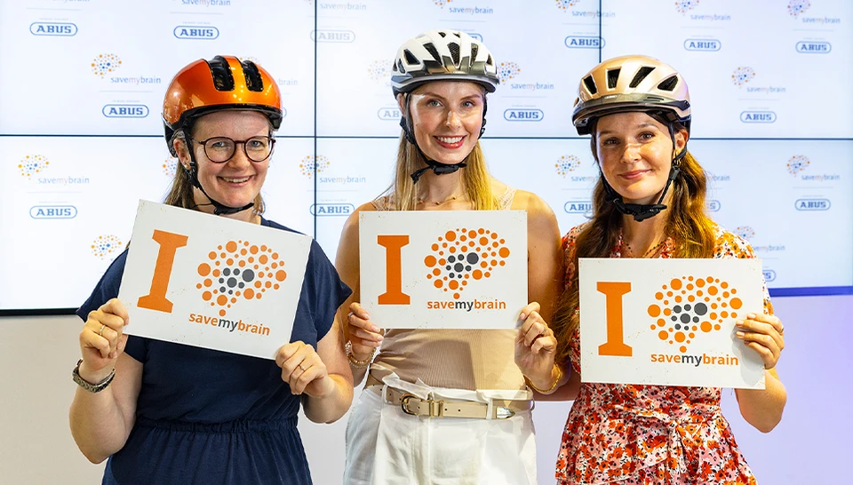 Drei ABUS Mitarbeiterinnen nebeneinander mit Fahrradhelm und einem Schild mit claim "I savemybrain" &copy; ABUS
