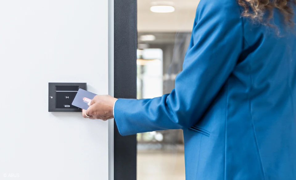 Une femme lit sa carte avec les autorisations d'accès sur le lecteur mural TECTIQ.