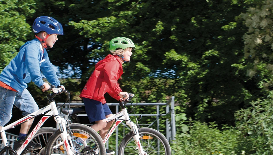 Zwei Kinder radeln im Park und tragen ABUS Youn-I MIPS Kinderhelme © ABUS