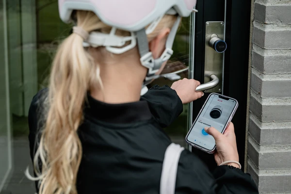 En cyklist &aring;bner en d&oslash;r med et elektronisk ABUS-d&oslash;rl&aring;s via sin smartphone. &copy; ABUS