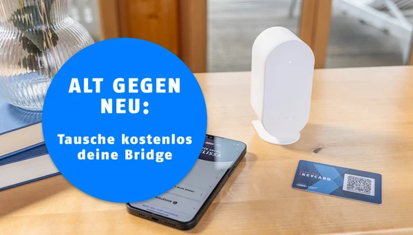 Text auf dem Bild: "Alt gegen neu: Tausche kostenlos deine Bridge", Bild: Auf einem Tisch steht die BRIDGE One, eine Keycard und ein Smartphone mit der ABUS One App &copy; ABUS