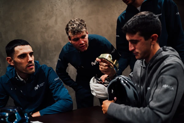 Vier Profirennradfahrer vom Movistar Team sitzen und stehen an einem Tisch und begutachten mehrere Modelle des AirBreaker 2.0 &copy; ABUS